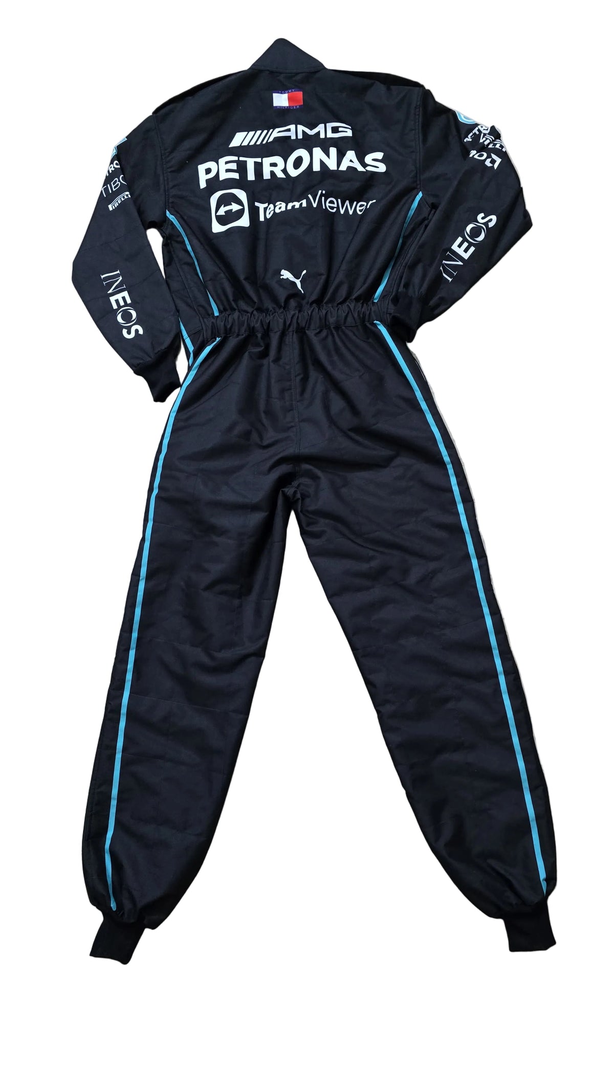 A black Puma Mercedes-AMG racing tracksuit with white and light blue sponsor logos and side stripes, laid flat on a beige marble floor.